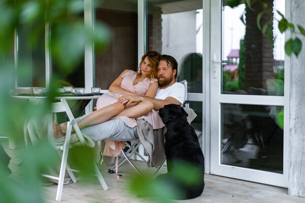 Ein Paar sitzt gemütlich auf einer Terrasse, begleitet von einem schwarzen Hund.